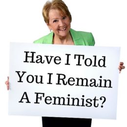 Patricia Morgan holding a sign, Have I Told You I Remain a Feminist? 