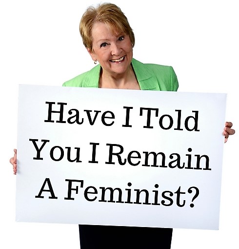 Patricia Morgan holding a sign, Have I Told You I Remain a Feminist? 